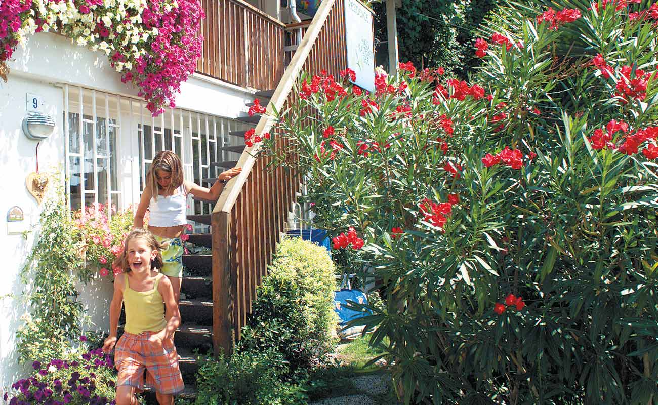 Großer Oleander mit roten Blüten neben der Holztreppe, welche die Terrasse vom Residence Haus Kalterer See mit dem Garten verbindet