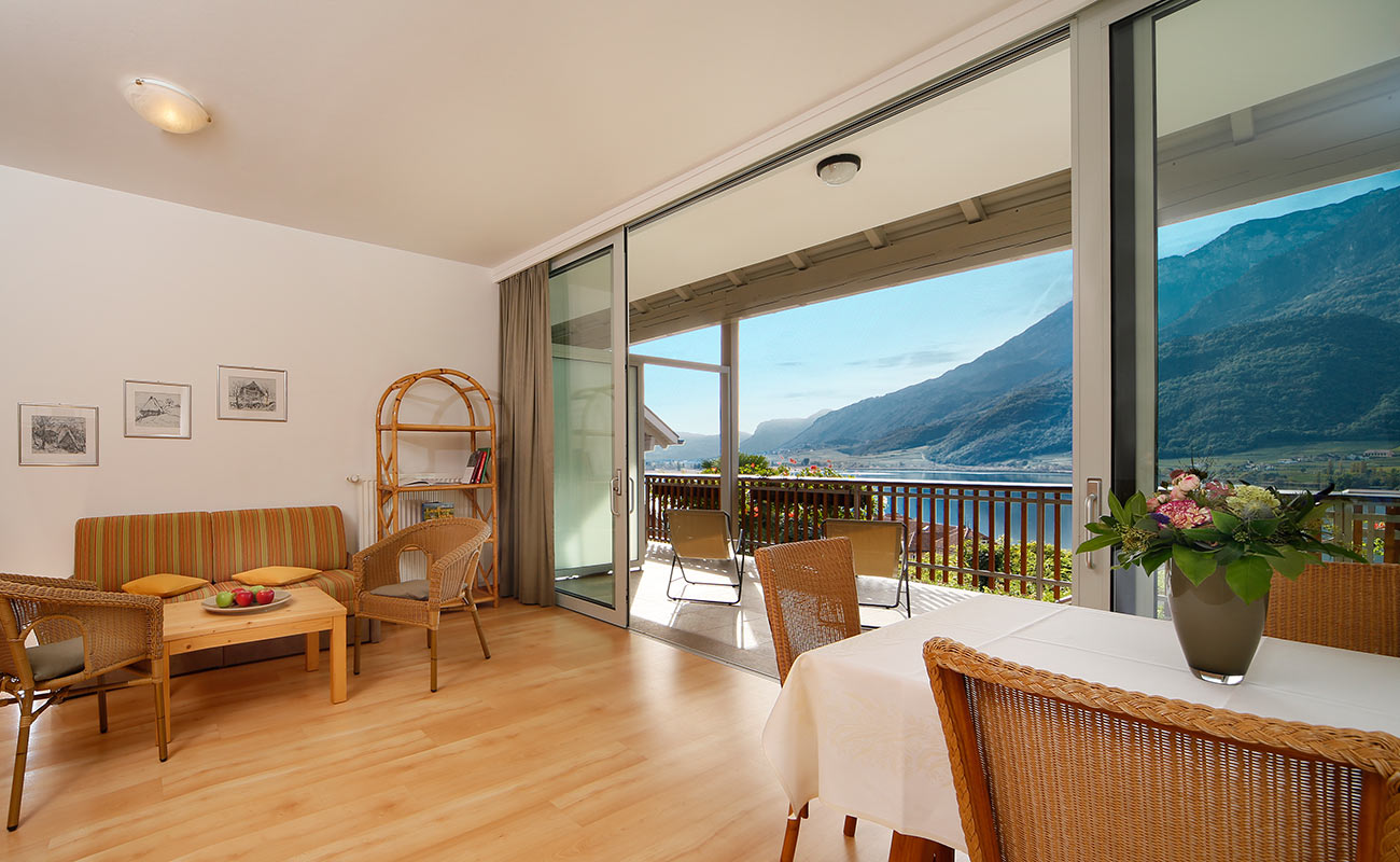 Der Wohnraum eines Apartments im Residence Haus Kalterer See mit Holzboden und großer Fensterfassade auf die Terrasse