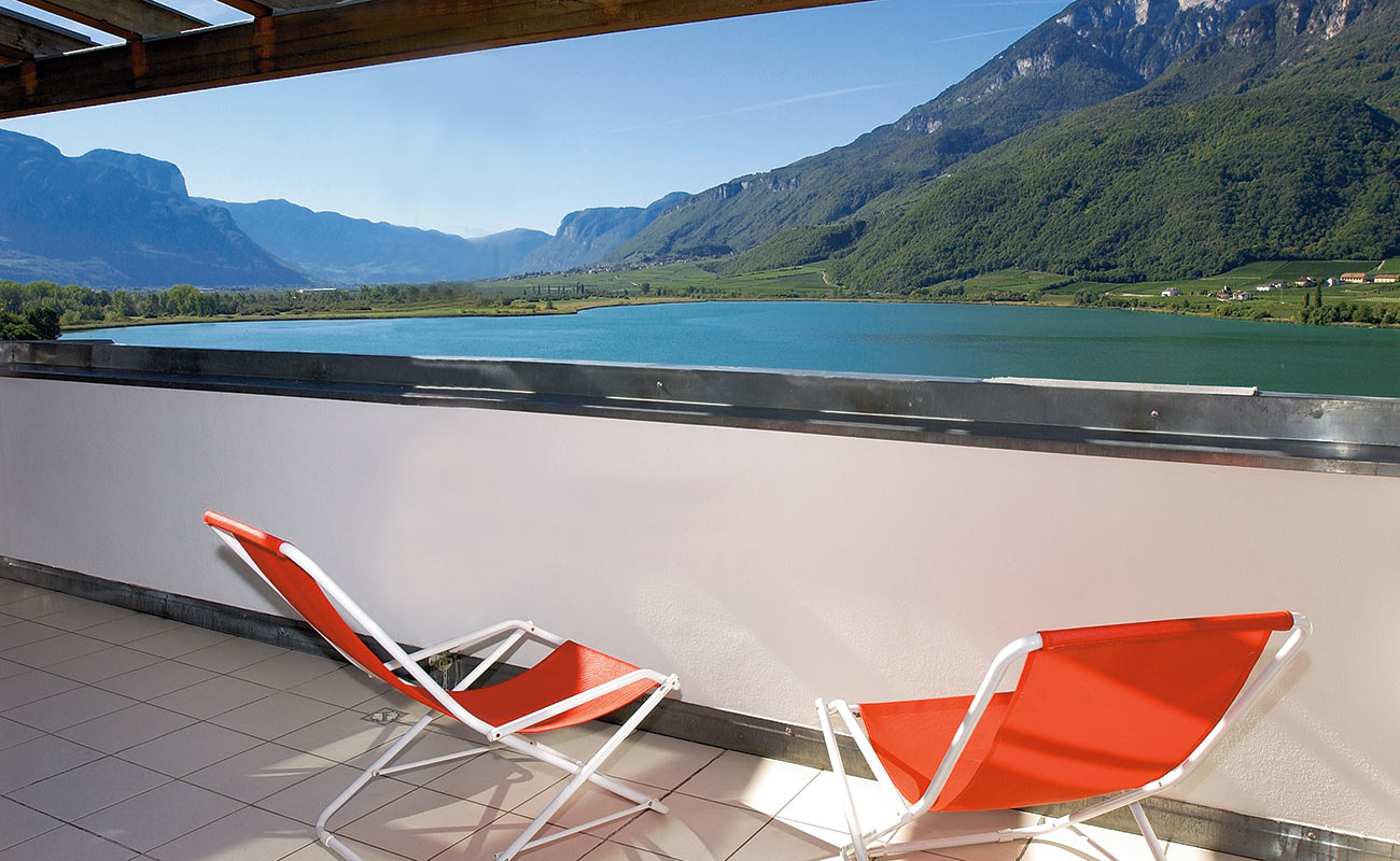 Zwei rote Liegestühle auf einer Terrasse im Residence Kalterer See mit Aussicht auf den See
