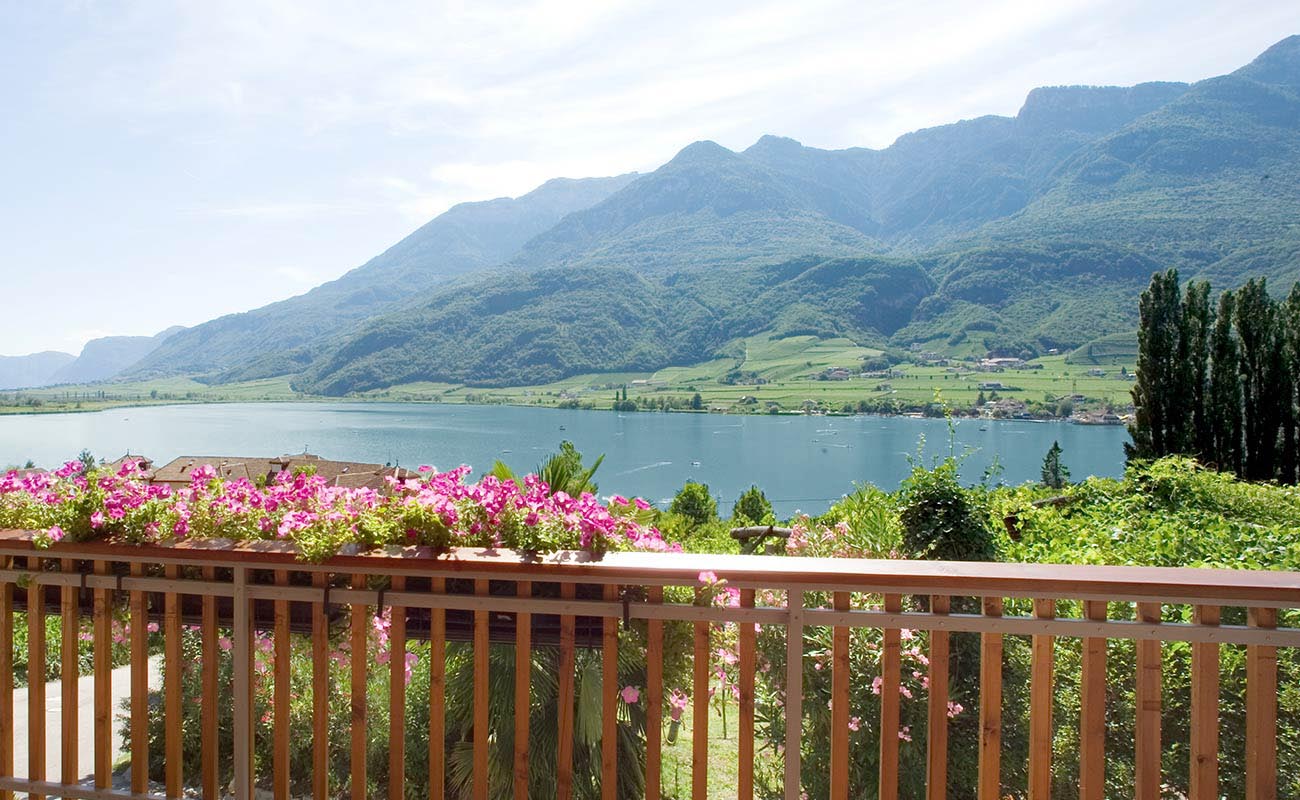 Aussicht auf den See von der Terrasse, mit Holzgeländer und violetten Petunien, vom Residence Haus Kalterer See